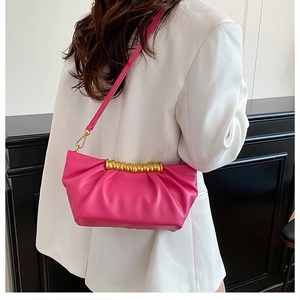 Detail shot of a vibrant pink pleated shoulder bag with gold metal handle on a fashion model