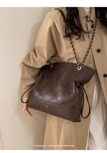 Detail of coffee brown quilted leather tote bag with gold chain strap on beige coat