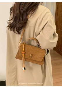 Detail of a brown matte suede handbag featuring a vintage gold twist lock and beaded tassel