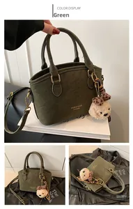 Detail of green suede crossbody bag with metal chain and plush bear charm accent