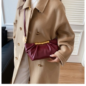Detail of burgundy ruched clutch bag with gold handle held by model in khaki coat