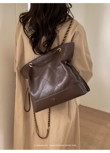 Detail of dark brown quilted tote bag with chain strap on khaki trench coat