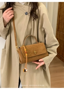 Brown faux suede tote bag with golden metal buckle and retro beaded tassel on a beige coat