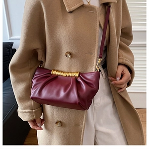 Detailed view of wine red pleated clutch bag with gold metal hardware worn with a coat