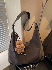 Brown suede hobo tote bag with a soft plush dog pendant in a cozy indoor setting