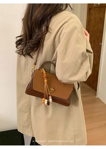 Retro two-tone crossbody bag with wooden bead tassel shown on a stylish trench coat