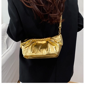Detail of gold metallic cloud bag with pleated texture and thin shoulder strap worn by model