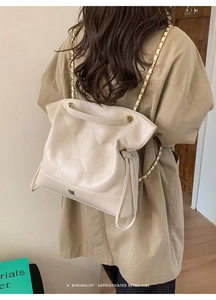 Quilted cream tote bag with gold chain strap styled on a khaki trench coat