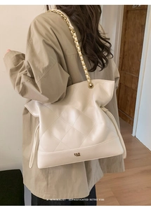 Lifestyle view showing the beige quilted tote bag with chain strap on a model's shoulder