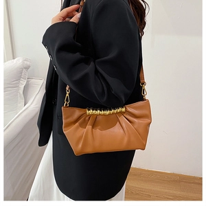 Detail of caramel pleated cloud bag featuring golden spiral metal hardware and strap