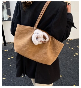 Detailed view of caramel brown suede tote bag with white stitching and rabbit charm