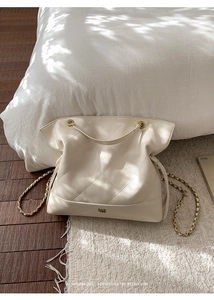 Detailed close-up of cream white quilted tote bag with chain strap and metal logo accent
