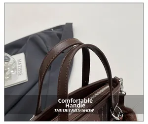 Détail du sac seau en cuir marron avec double poignée, fermeture éclair et pompon en peluche