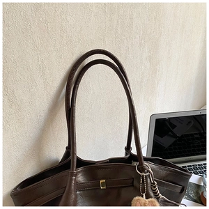 Detail of a dark brown pleated leather tote bag with a gold buckle and fuzzy ball charm