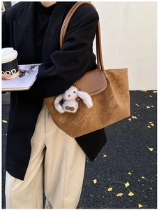 Detail of a brown suede tote bag with a leather strap and a cute rabbit plush charm detail