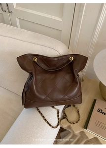 Detail of dark brown quilted leather tote bag with golden chain strap and round metal handle