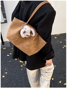 Close-up of brown suede tote bag with cute plush rabbit charm on a street setting