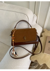 Detail of retro dual-texture dark brown leather bag with golden clasp and beaded charm