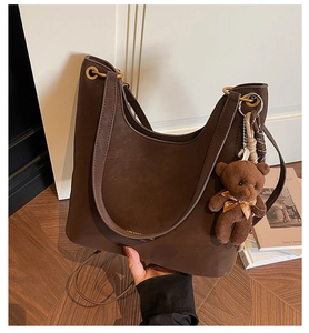Close-up of deep brown Hobo tote bag with golden metal rings and cute bear plush charm