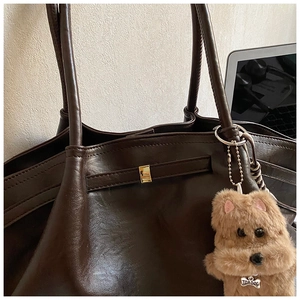 Close-up of deep brown leather tote with a gold buckle and cute plush dog pendant