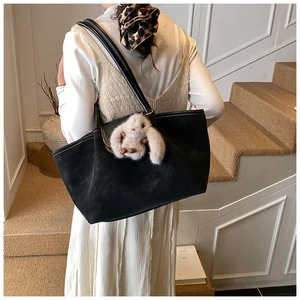 Close-up of black suede tote bag with white stitching detail and plush rabbit charm