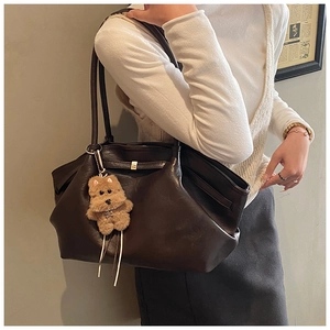 Detail of dark brown pleated tote bag with sleek metal buckle and plush puppy charm