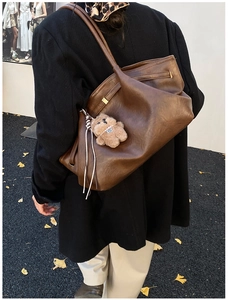 Deep brown oversized tote bag detail with plush bear charm and decorative ribbon