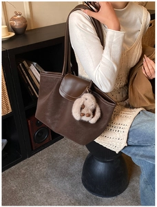 Detail view of brown leather tote bag with contrast stitching and plush bunny charm