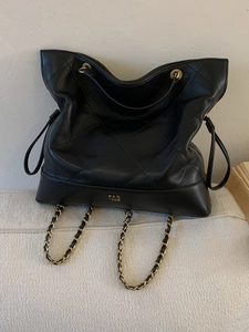 Quilted black leather tote bag with gold chain straps for commuting on beige sofa