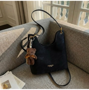 Detail of black leather crescent tote with logo and plush bear charm on a sofa