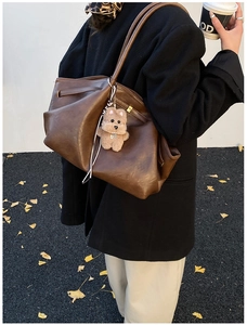 Detail of dark brown pleated tote bag with a cute plush puppy charm in autumn setting