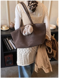Detail of dark brown tote bag with white contrast stitching and plush rabbit charm