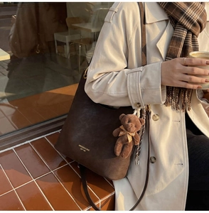 Detail of dark brown matte leather tote bag featuring a cute teddy bear charm and logo