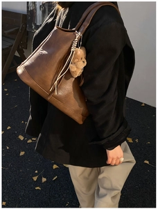Detail of large brown leather tote bag with teddy bear charm on winter wool coat