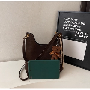 Detail of dark brown leather hobo bag with gold hardware, plush bear charm and tablet