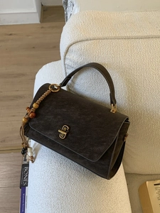 Vintage dark grey matte leather handbag with golden clasp and tassel on a white sofa