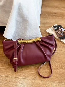 Burgundy pleated leather crossbody bag with golden spiral metal handle on wooden floor
