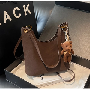 Detail of dark brown matte leather tote with golden hardware and plush bear charm