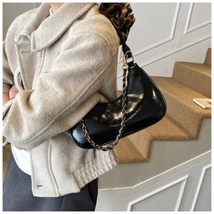 Detail of black glossy crescent bag with gold chain strap on light wool coat