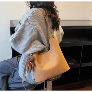 Detail of camel leather tote featuring a metal ring buckle and plush bear pendant