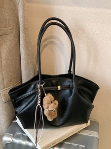 Large black leather tote bag with plush bear charm and woven tassel on silver suitcase
