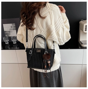 Sac seau noir chic à rayures verticales et pompon marron sur une table en bois