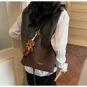 Detail of matte brown tote bag with bear charm and gold lettering on premium leather