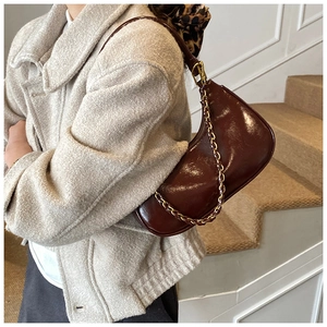 Detail of dark brown glossy patent leather shoulder bag with gold chain and strap