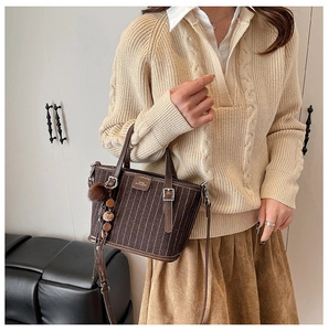 Détail du sac cabas à rayures marron foncé avec pompon en peluche et breloque à glands