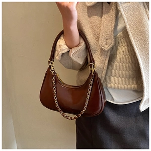 Detail of glossy brown crescent bag with luxury gold chain and sleek polished texture