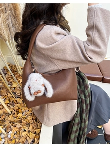 Detail of dark brown pebble leather hobo bag with white bunny plush charm in autumn setting
