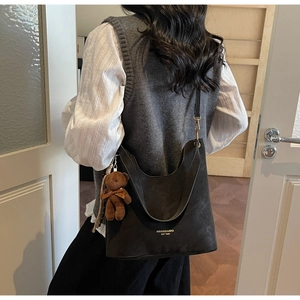 Detail of black tote bag with gold lettering and brown bear pendant worn by a model