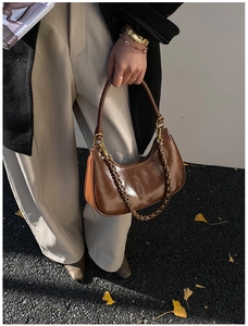 Close-up of brown glossy moon bag with stylish metal chain and smooth leather handle