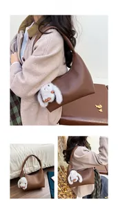 Detail view of brown pebbled leather hobo bag with a white rabbit plush keychain accessory